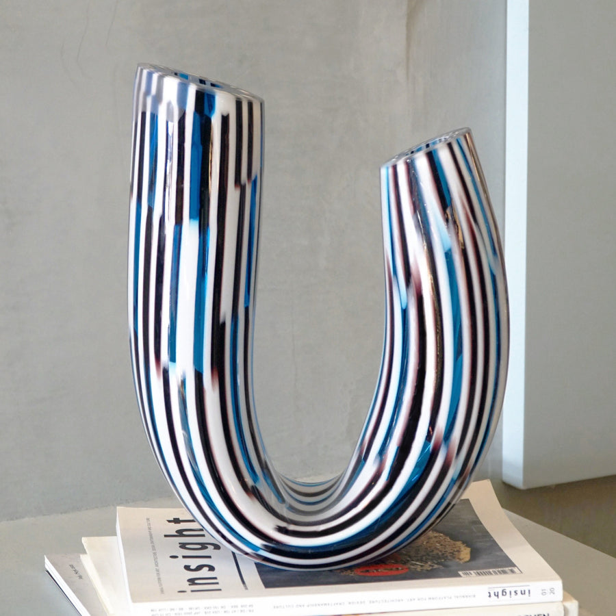 The Boomerang Twid is a unique vase designed by Marco Mencacci and realized in Murano. Mencacci can transform the material of glass into plasma, evoking the living world of the abyss, tribal rituals, the reflections of oil or latex, the transparencies of sea creatures and the pearliness of shells. 